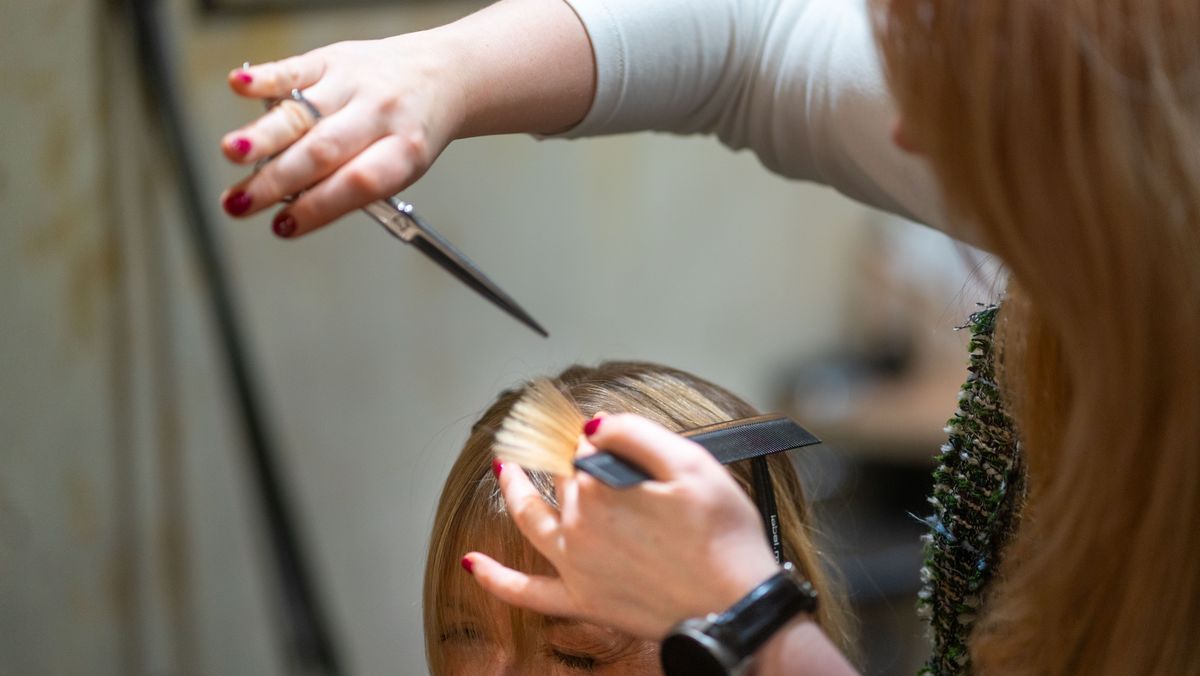 Stylistin arbeitet mit Schere und Kamm am Deckhaar einer Kundin