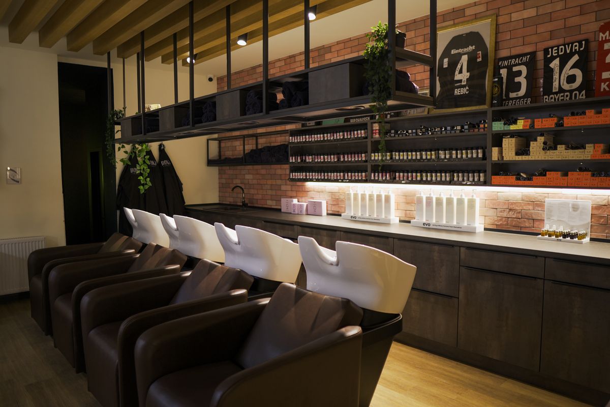 Wartebereich im Boki Salon in der Großen Seestraße in Frankfurt-Bockenheim mit Ziegelwand, Pflegeprodukten im Regal und signierten Trikots
