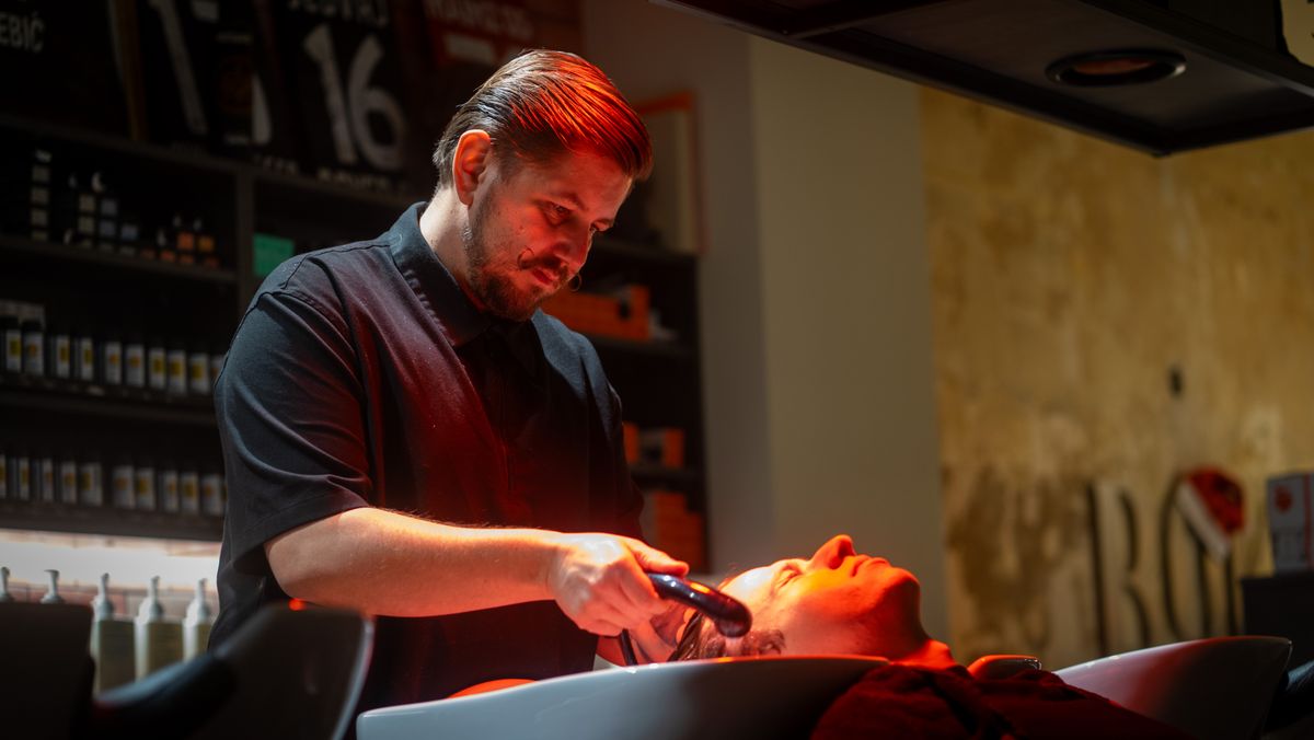 Stylist arbeitet am Waschplatz unter der Wärmelampe eine Farbe ein